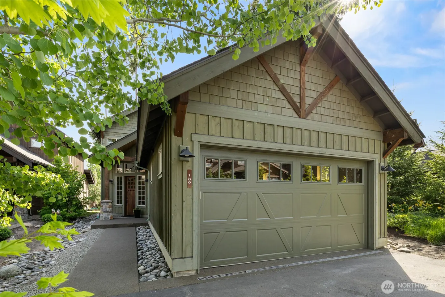 Exterior of a green house with a garage door, stone walkway, and green trees.