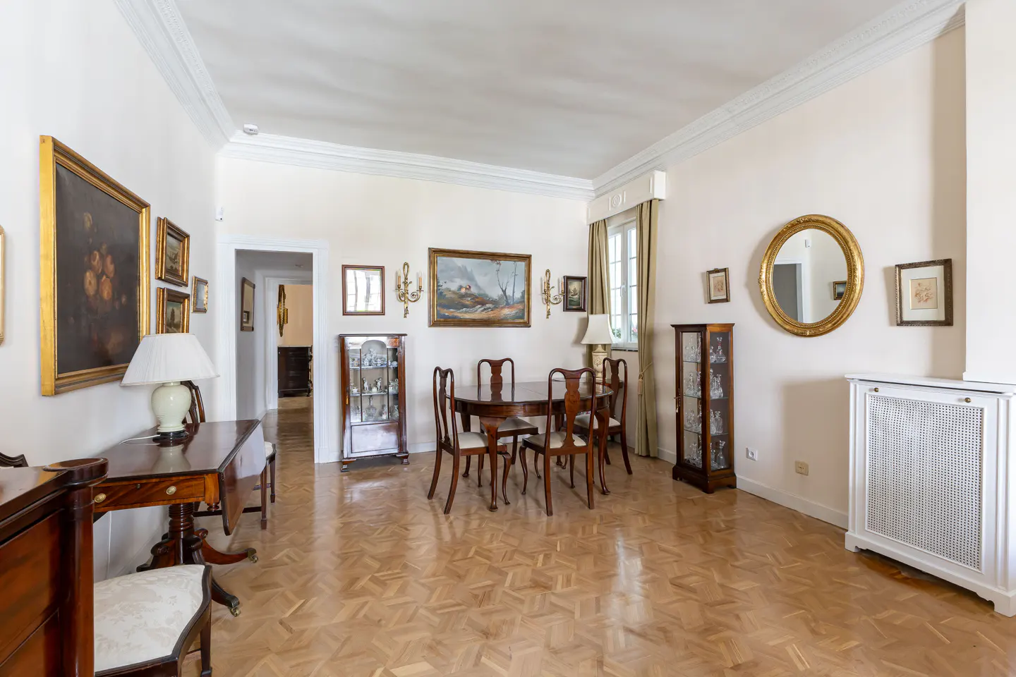 A bright, elegant dining room with parquet floors, a round table with chairs, and framed artwork on the walls.