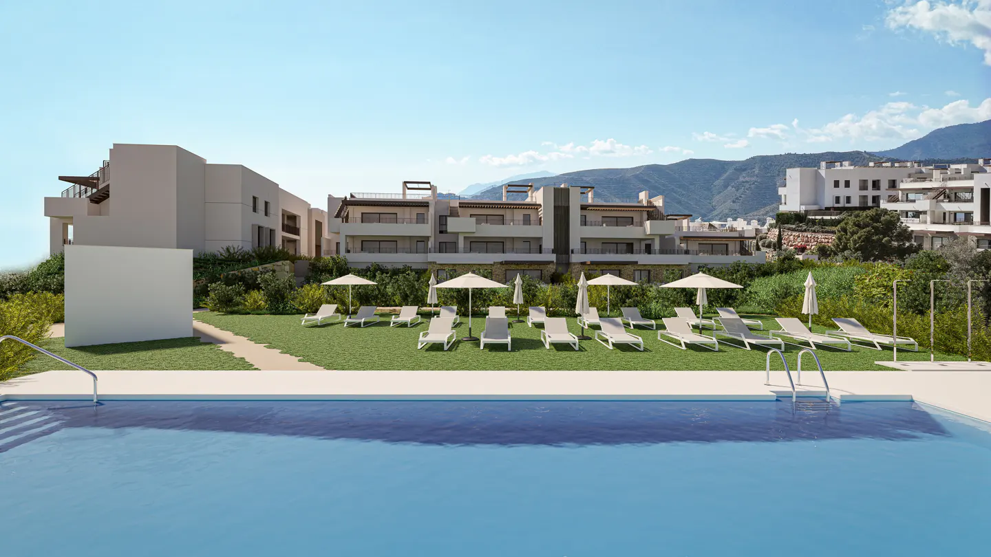 Exterior view of a modern apartment complex with a pool, lounge chairs, and mountain backdrop on a sunny day.