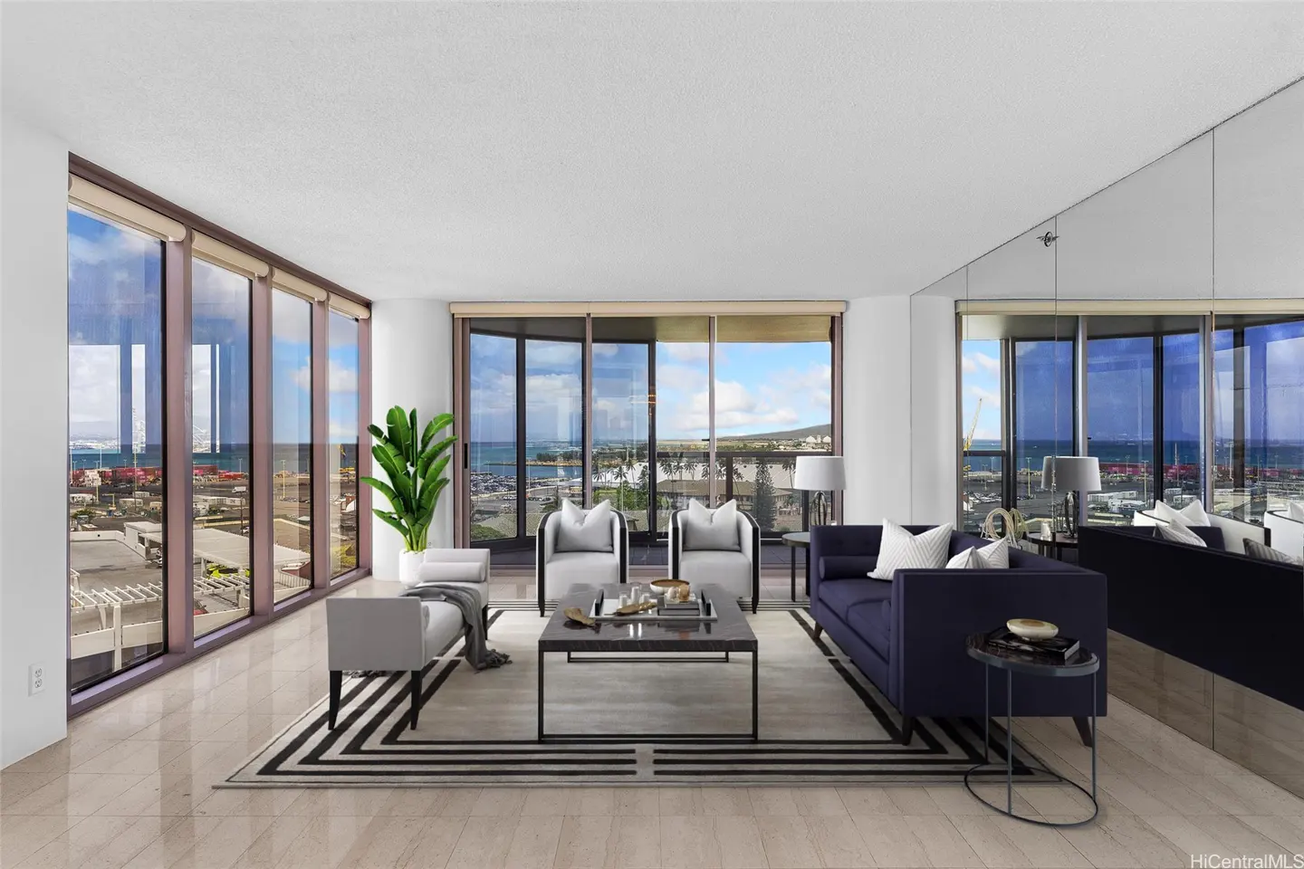 Modern living room with a navy sofa, two white armchairs, and a coffee table, featuring floor-to-ceiling ocean views.