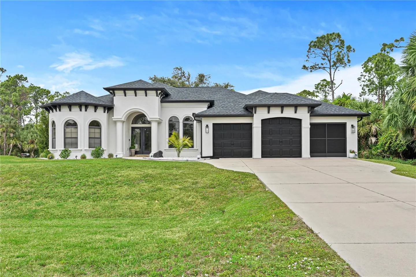 A white, one-story house with a dark roof and three-car garage sits on a green lawn under a blue sky.