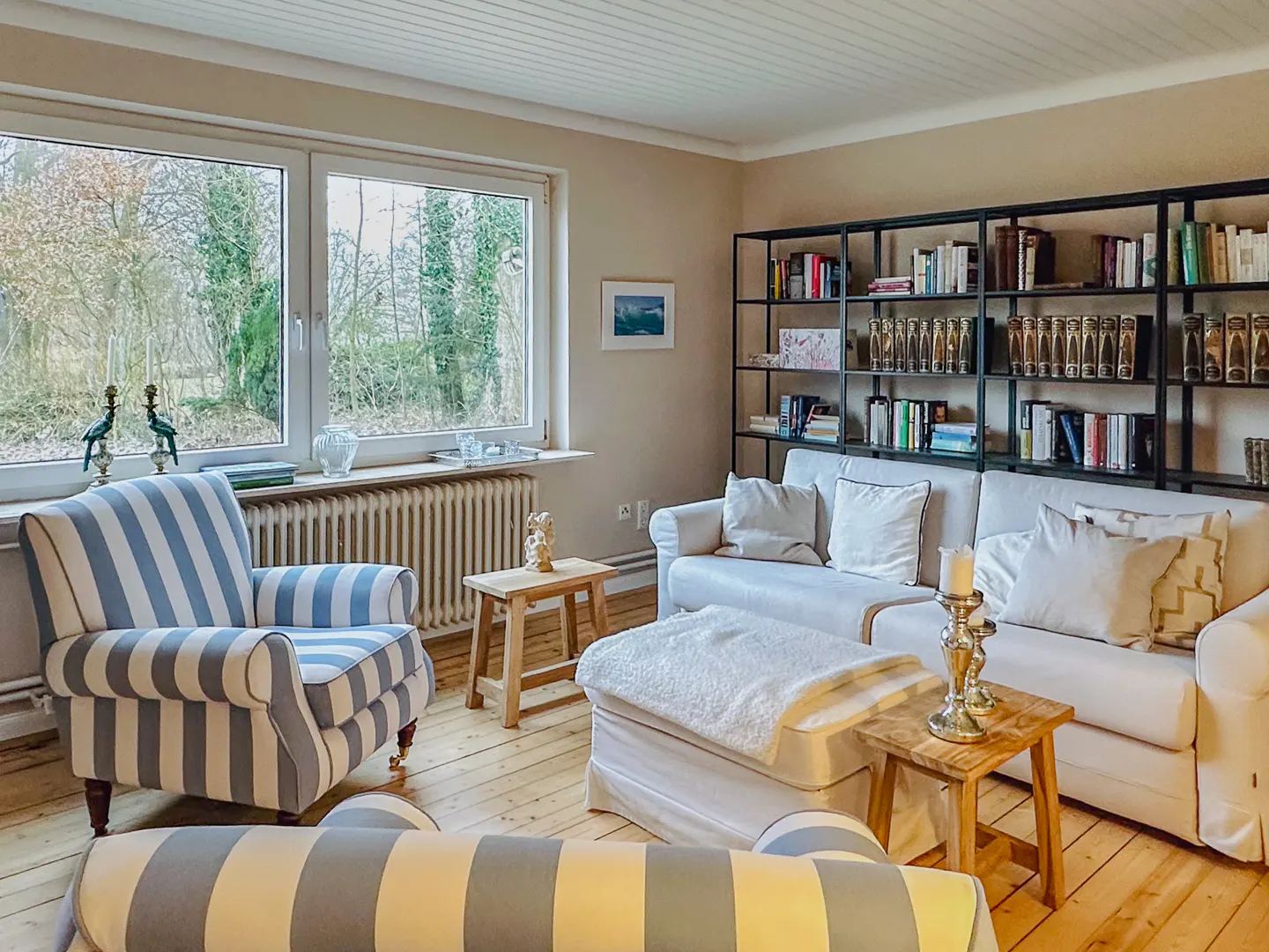 Living room with a white sofa, striped armchair, wooden floor, and a black bookshelf filled with books.