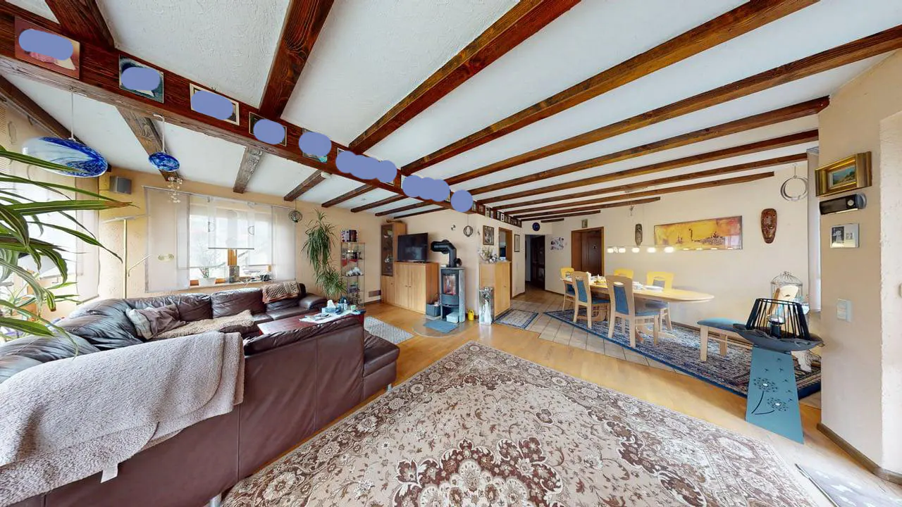 A living room with a brown leather sofa, a dining table with yellow chairs, and exposed wooden beams on the ceiling.