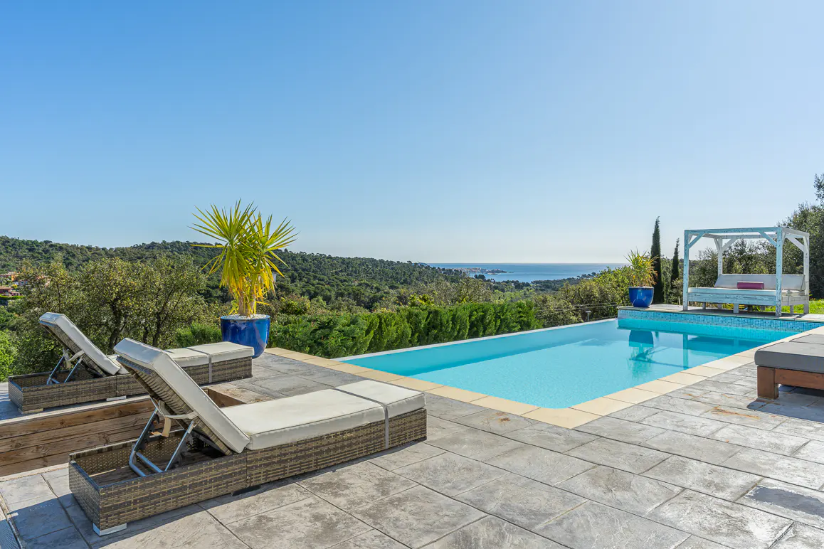 A bright, sunny day at a luxury villa with a pool, lounge chairs, and ocean view.