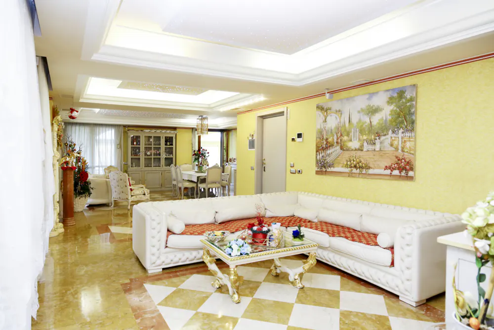 A bright living room with yellow walls, a white sofa, and a painting of a garden scene.