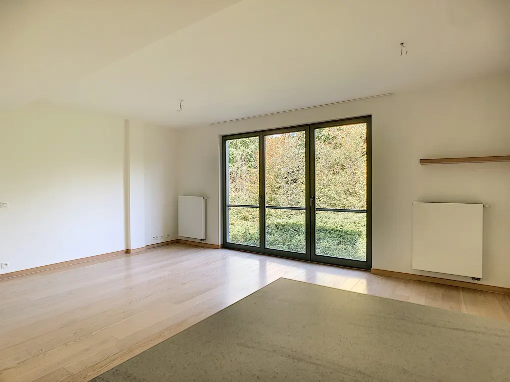 Bright, empty room with light wood floors, white walls, and a large sliding glass door to a green outdoor space.