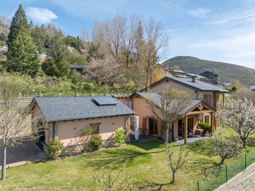 Exterior view of a peach-colored house with a gray roof, stone accents, and a green lawn in a mountainous area.