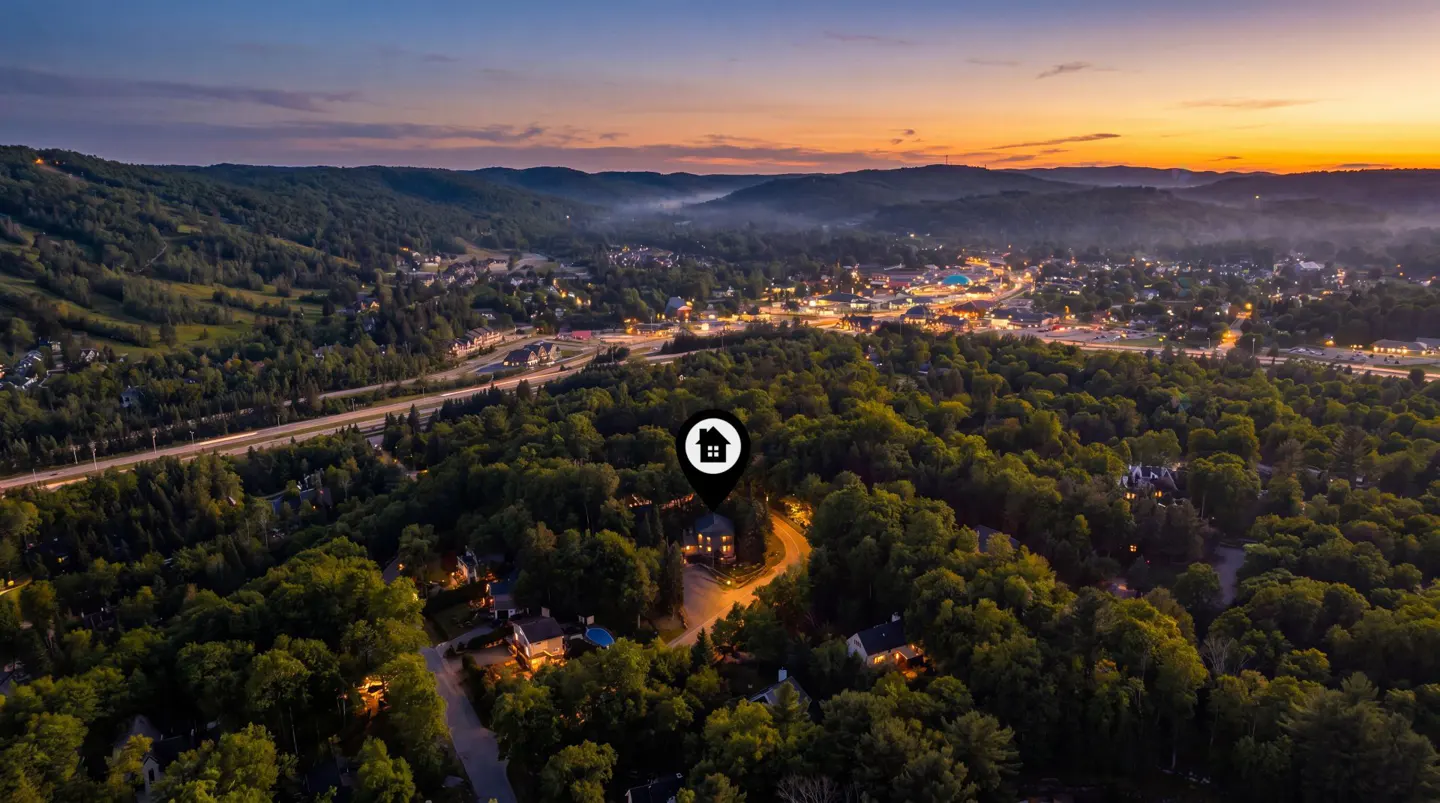 Aerial view of a home nestled in a forest at sunset, marked with a house icon pin. Distant city lights glow.