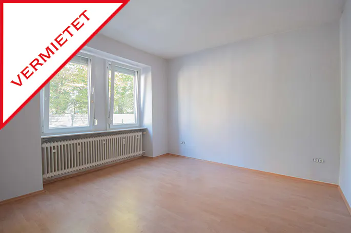 Empty room with light wood floor, white walls, radiator under a window, and a red "VERMIETET" banner.