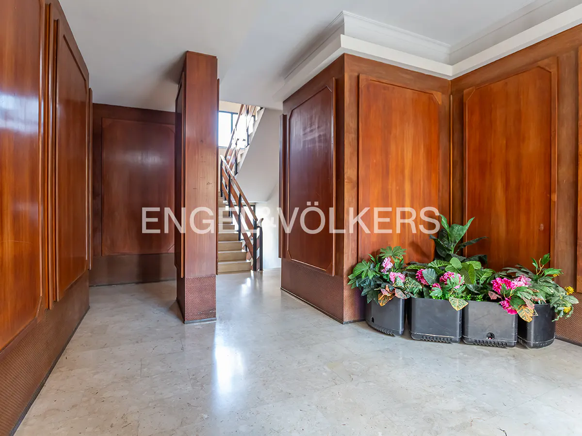 Interior shot of a foyer with wood paneling, marble floors, and potted plants. Stairs are visible in the background.