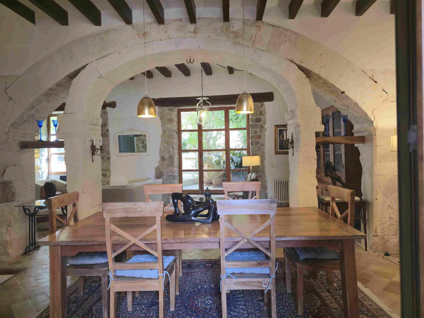 A dining room with a wooden table and chairs, stone arches, and pendant lights.