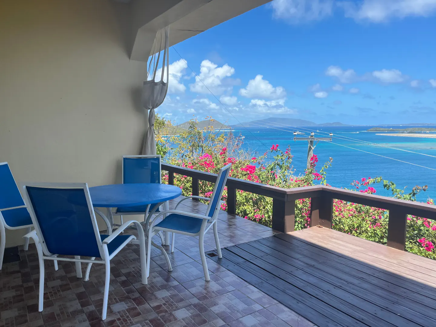 Outdoor patio with blue table and chairs overlooking a scenic ocean view with pink flowers.