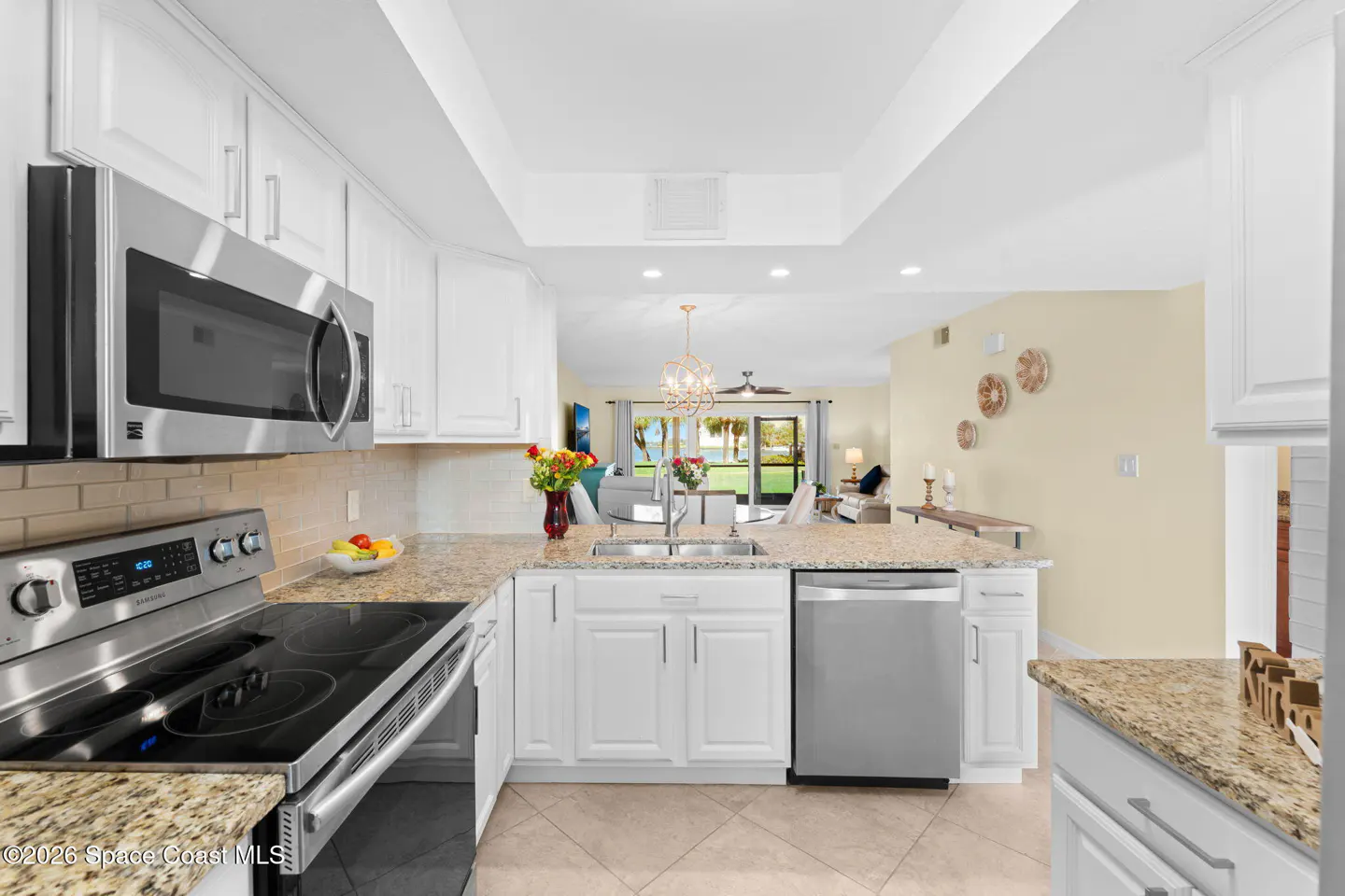 Bright kitchen with white cabinets, granite countertops, and stainless steel appliances. View to living room and ocean.