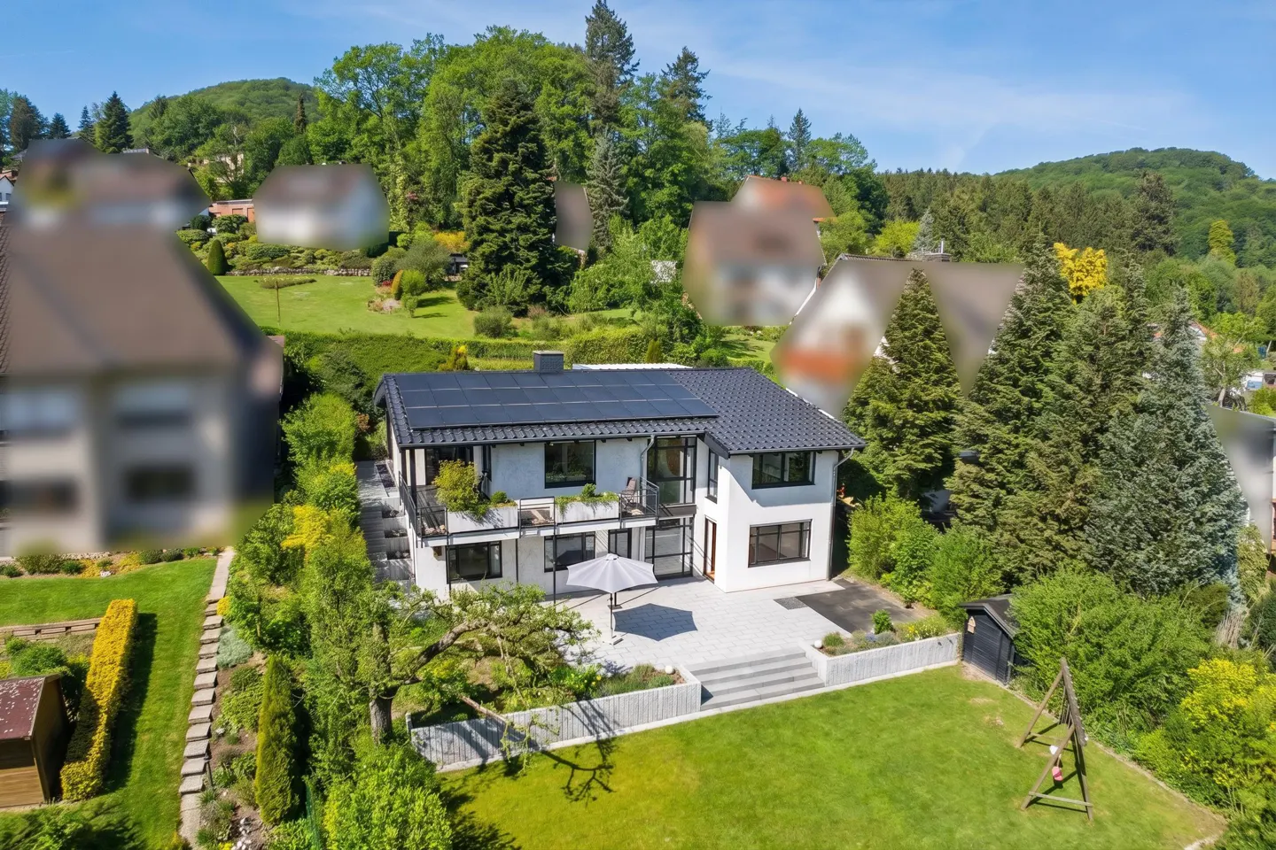 Two-story white house with black trim and solar panels, surrounded by green lawn and trees on a sunny day.