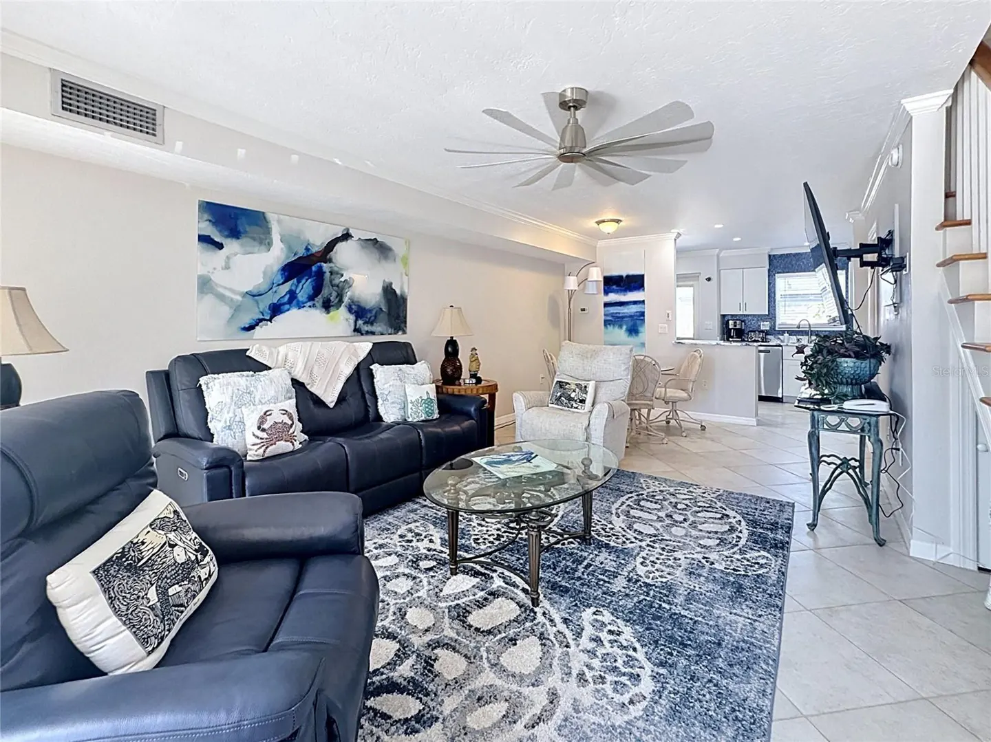 Open-concept living room with navy leather furniture, a turtle-patterned rug, and a view into a white kitchen.