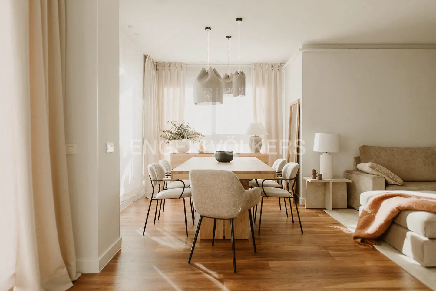 Bright, modern dining room with a wooden table, upholstered chairs, pendant lights, and a neutral color palette.