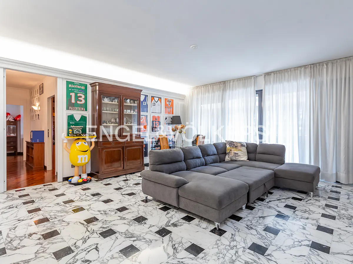 Living room with gray sectional sofa, marble floors, and sports memorabilia on the wall. A yellow M&M statue stands near a wooden cabinet.
