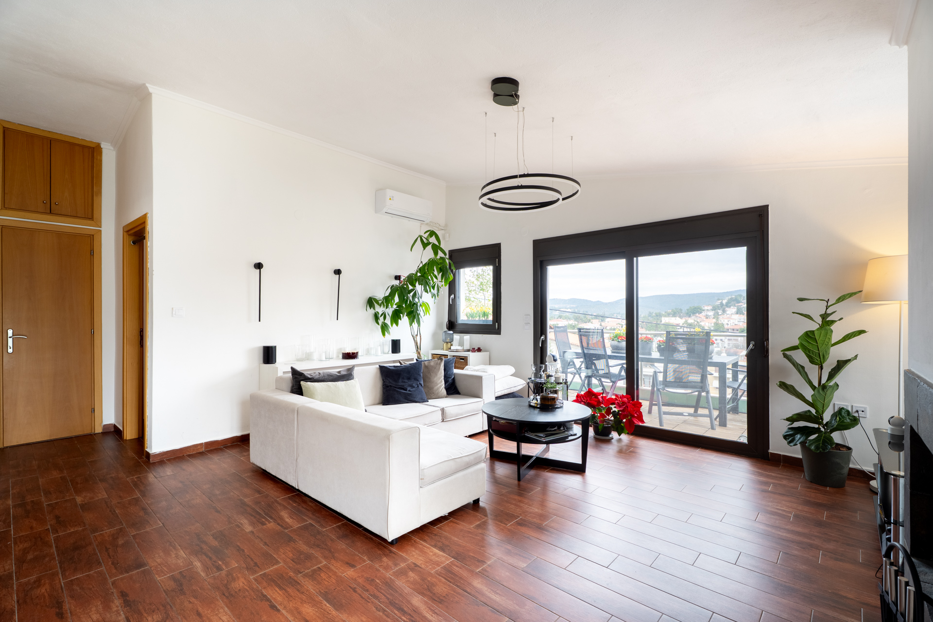 Bright living room with white walls, wood floors, and a white sofa. Sliding glass doors lead to a balcony with a view. [AI-generated text]