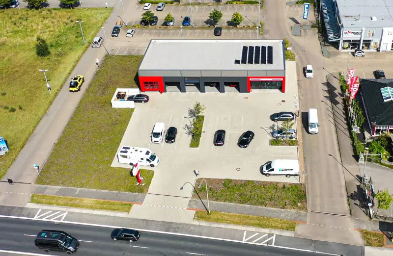 Aerial view of a gray and red auto shop with cars parked in front, and a road with cars in the foreground.
