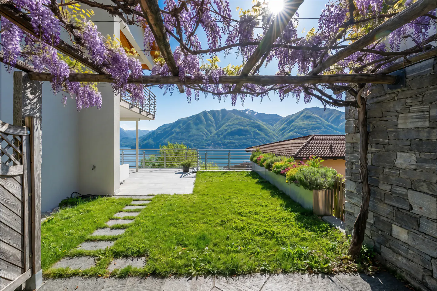 A backyard with a pergola covered in purple wisteria, a green lawn, and a mountain view.