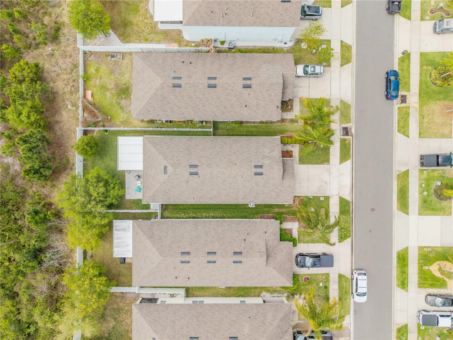 Aerial view of a residential neighborhood with beige houses, green lawns, and parked cars on a gray street.