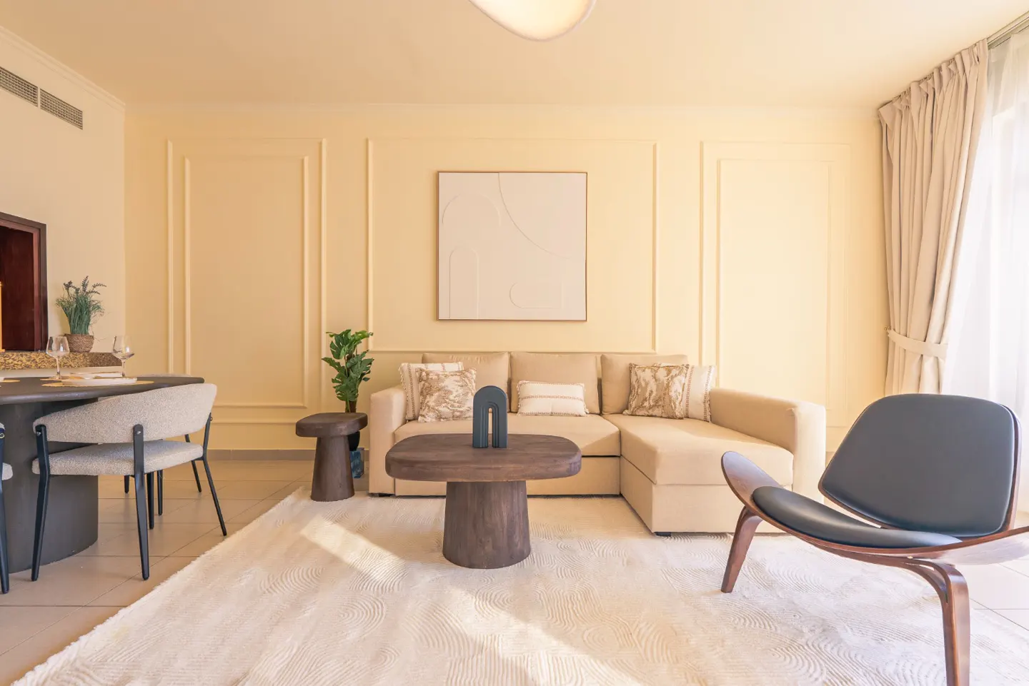 A bright living room with a beige sectional sofa, a wooden coffee table, and a gray chair on a cream rug.