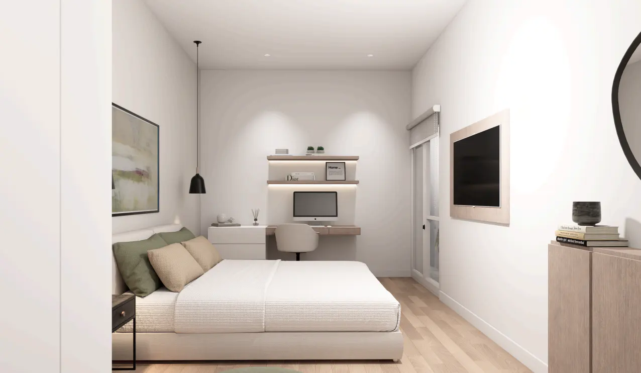 Bright bedroom with white walls, a bed with green and beige pillows, a desk with a computer, and a TV on the wall.