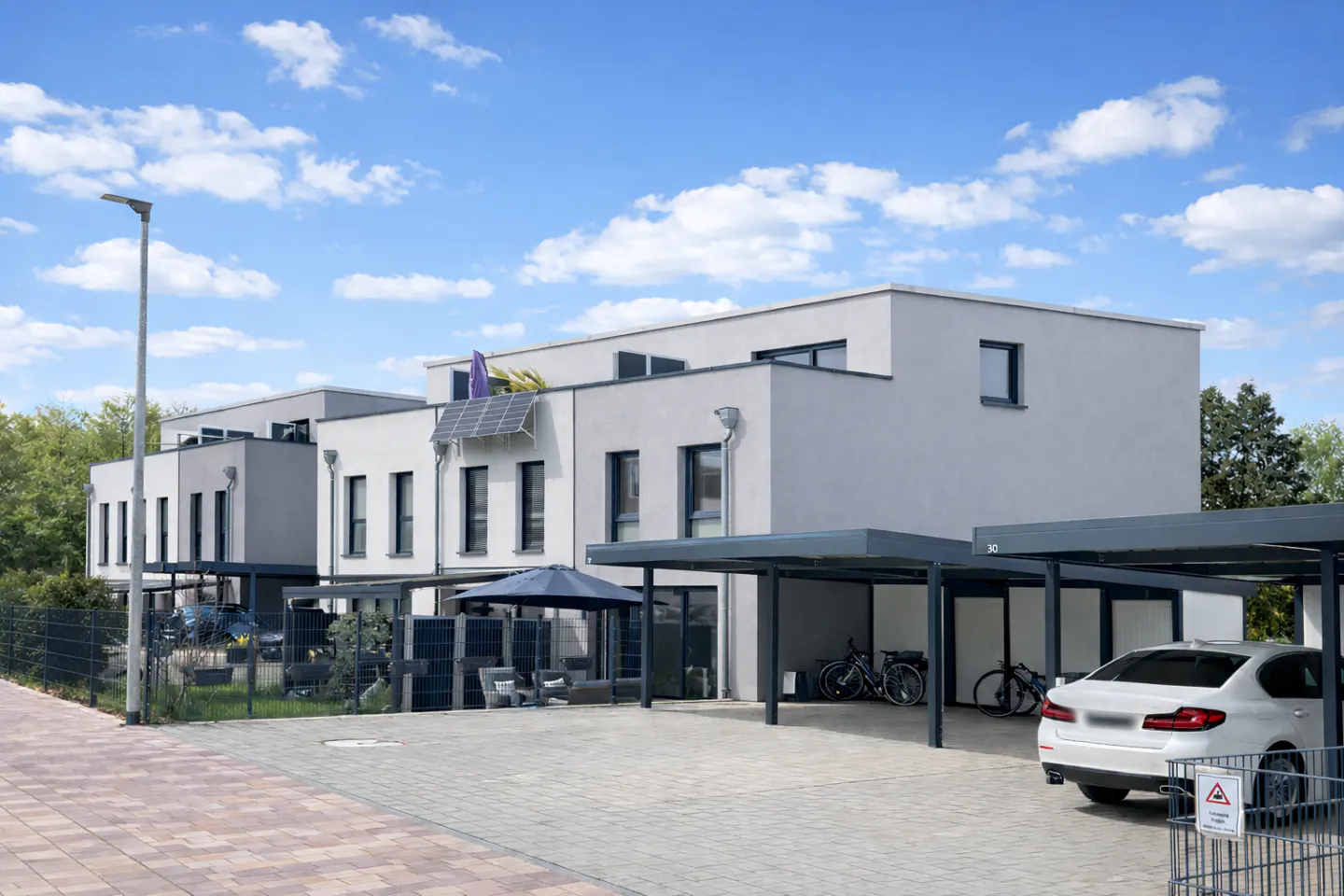 Modern townhouses with carports. Gray and white exteriors, solar panels, and a blue sky background.