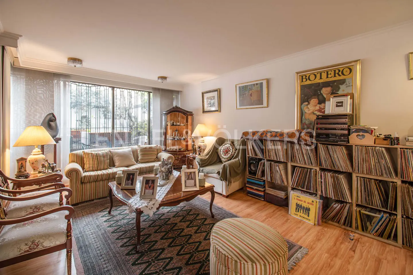 A living room with a striped sofa, wooden chairs, a coffee table with framed photos, and shelves filled with vinyl records.