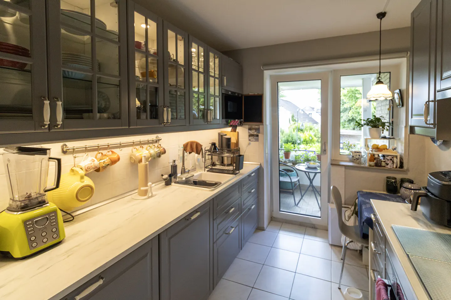 Modern kitchen with gray cabinets, white countertops, a bright yellow blender, and a glass door leading to a balcony.