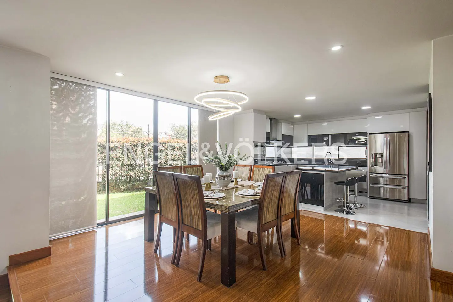 Open concept dining and kitchen area with wood floors, table set for eight, and stainless steel appliances.