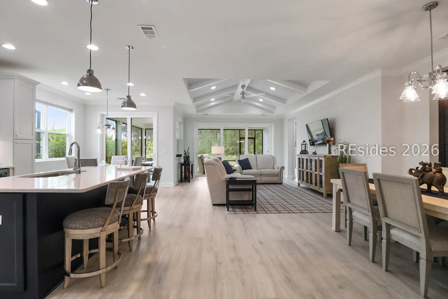 Open-concept living space with a kitchen island, bar stools, dining table, and living room with sofas and a TV.