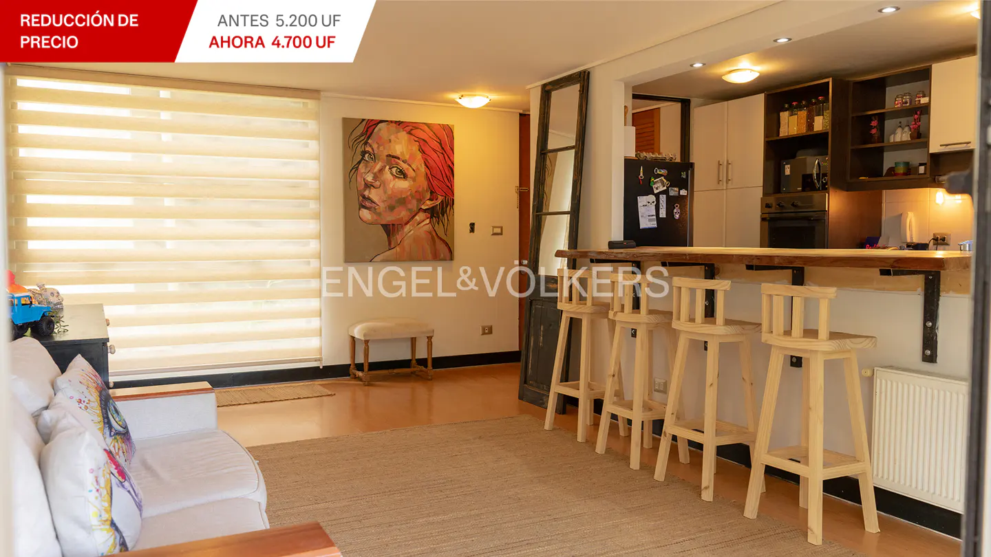Bright living room with a white sofa, a beige rug, and a wooden breakfast bar with four stools. A painting of a woman hangs on the wall.