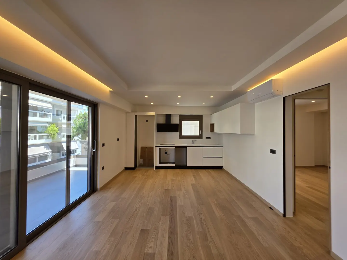 Modern open-plan kitchen with white cabinets, wood floors, recessed lighting, and a sliding glass door to a balcony.