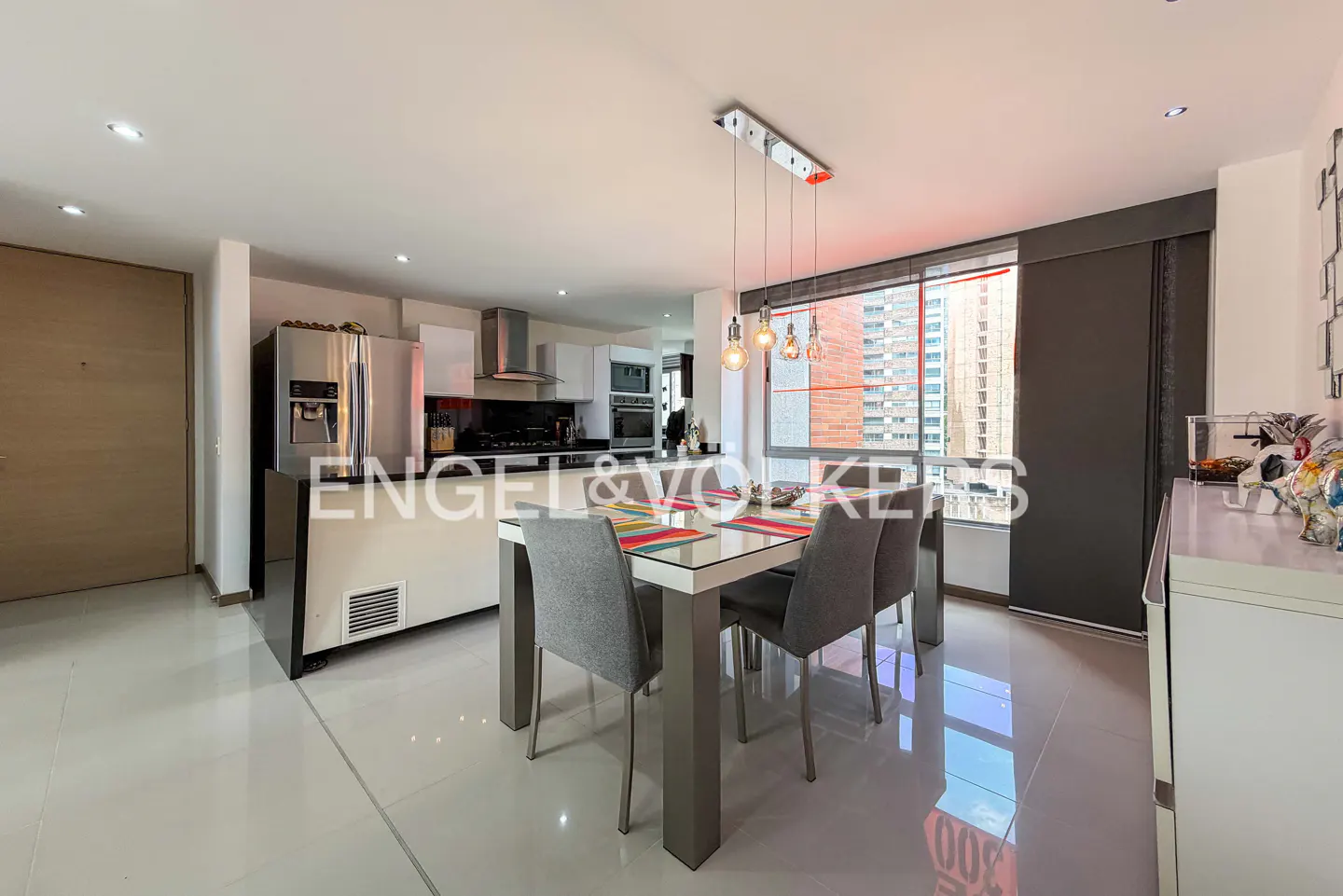 A modern kitchen and dining area with white cabinets, stainless steel appliances, and a glass-topped table with gray chairs. A large window overlooks a city skyline.