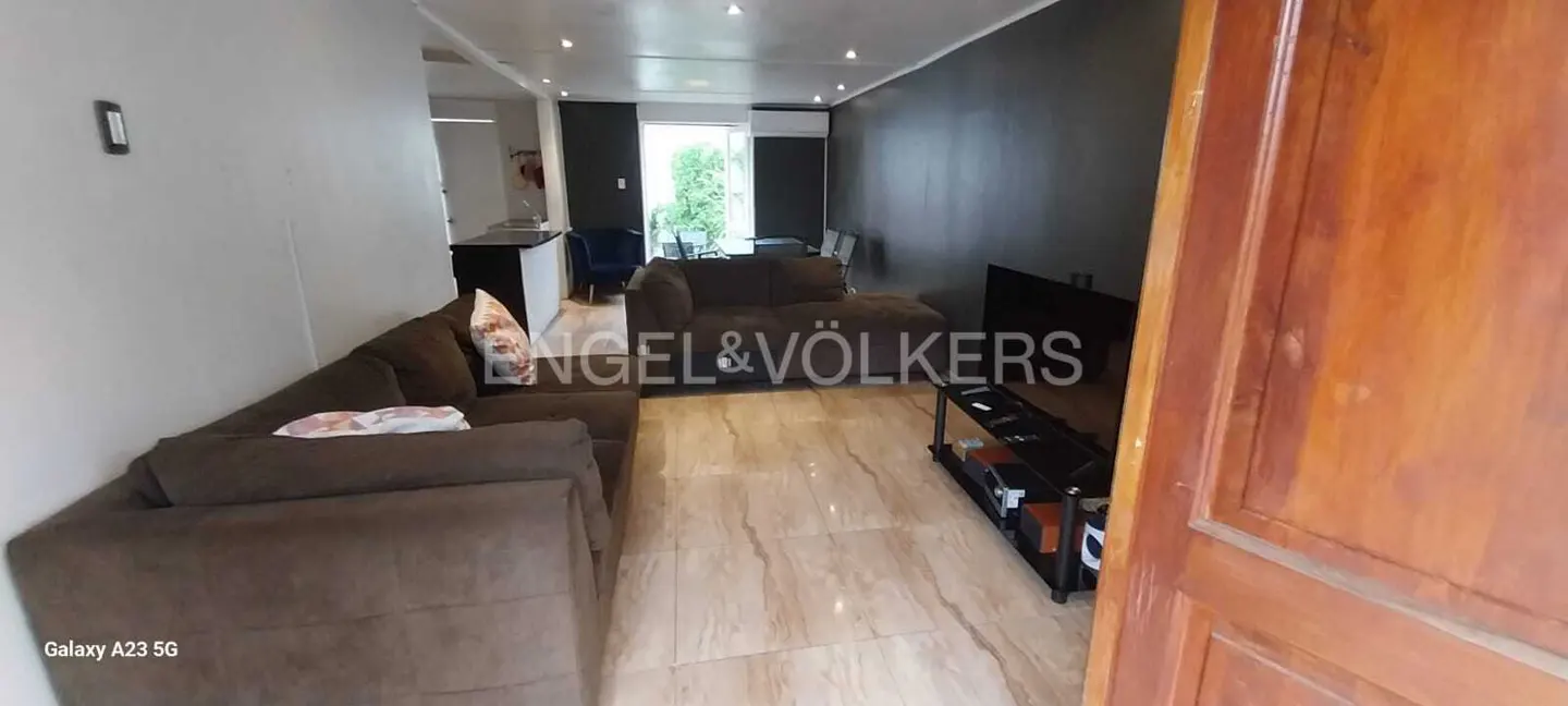A living room with brown sofas, a black TV stand, and marble floors, viewed from an open wooden door.