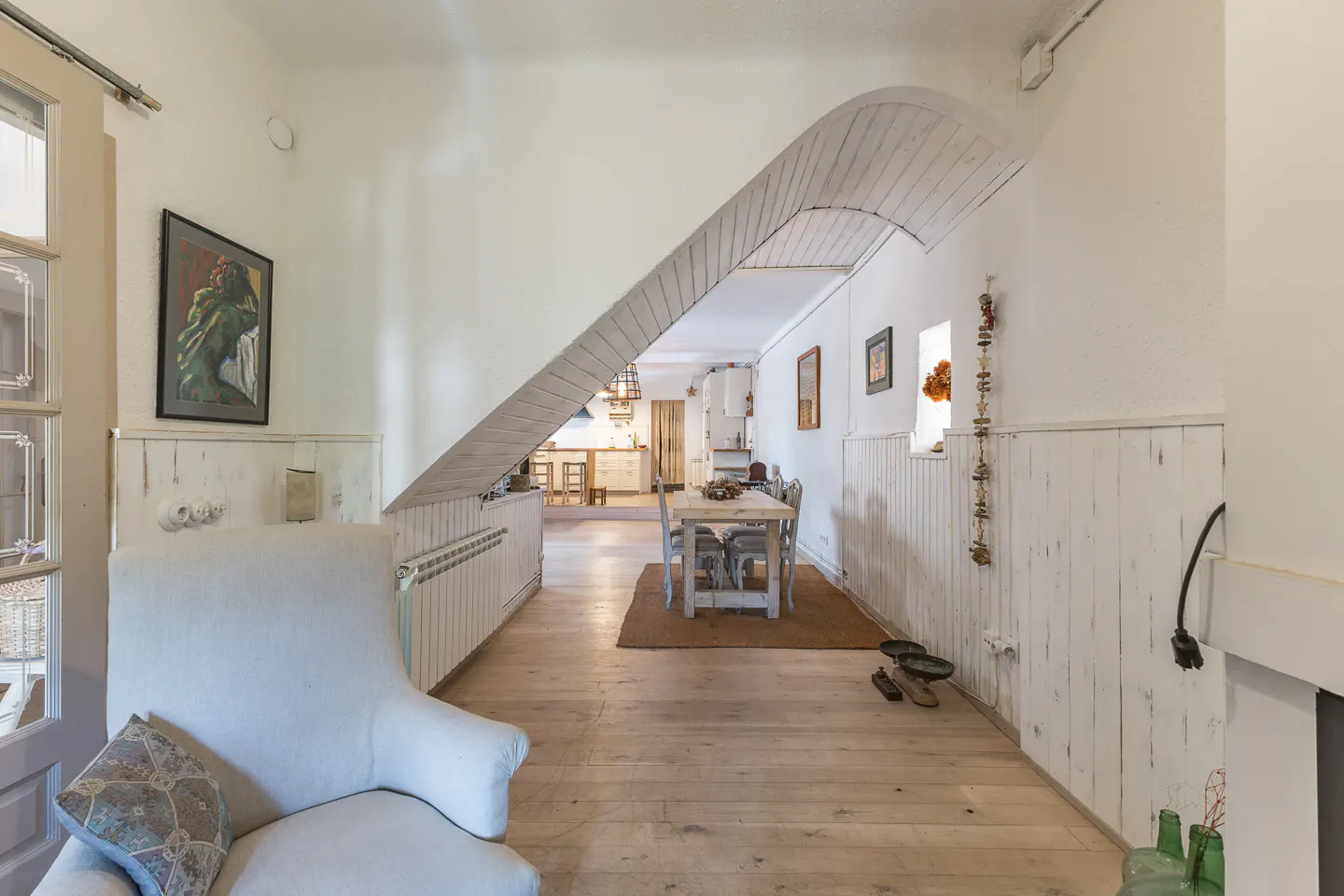 Bright, open-concept home interior with white walls, wood floors, and a dining area visible through an arched opening.