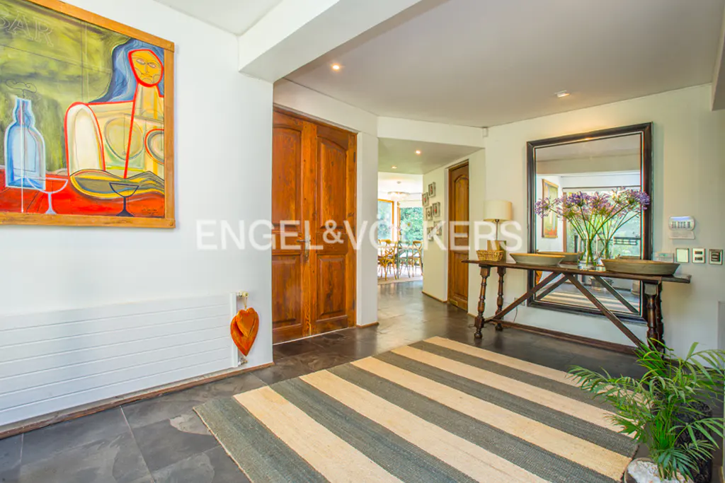 A home's entryway with a striped rug, a painting, and a wooden double door. A mirror reflects flowers on a table.