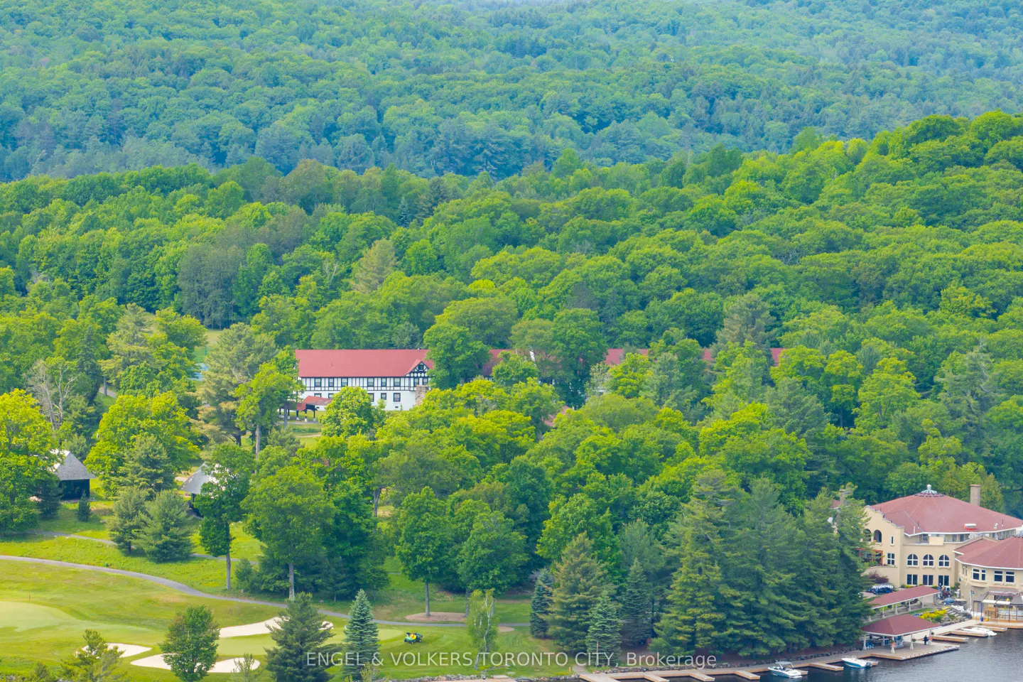 Aerial view of a large resort with a red roof nestled in a lush green forest next to a lake and golf course.