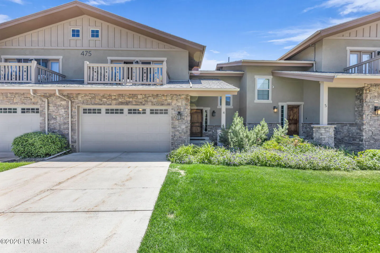 Exterior view of a two-story townhouse with stone siding, a concrete driveway, and a lush green lawn under a blue sky.