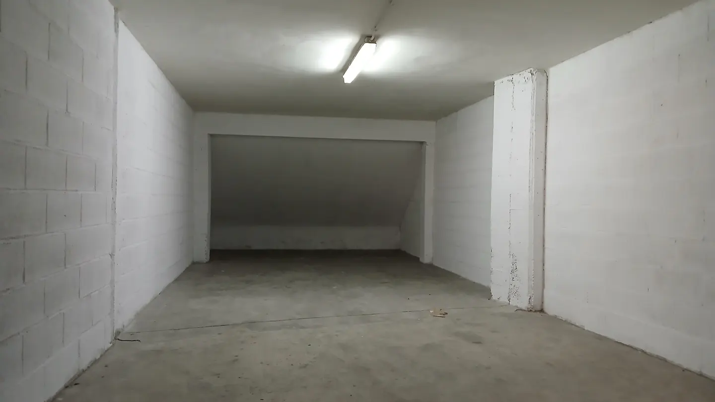 Empty, rectangular storage room with white painted cinder block walls, concrete floor, and a single overhead fluorescent light.