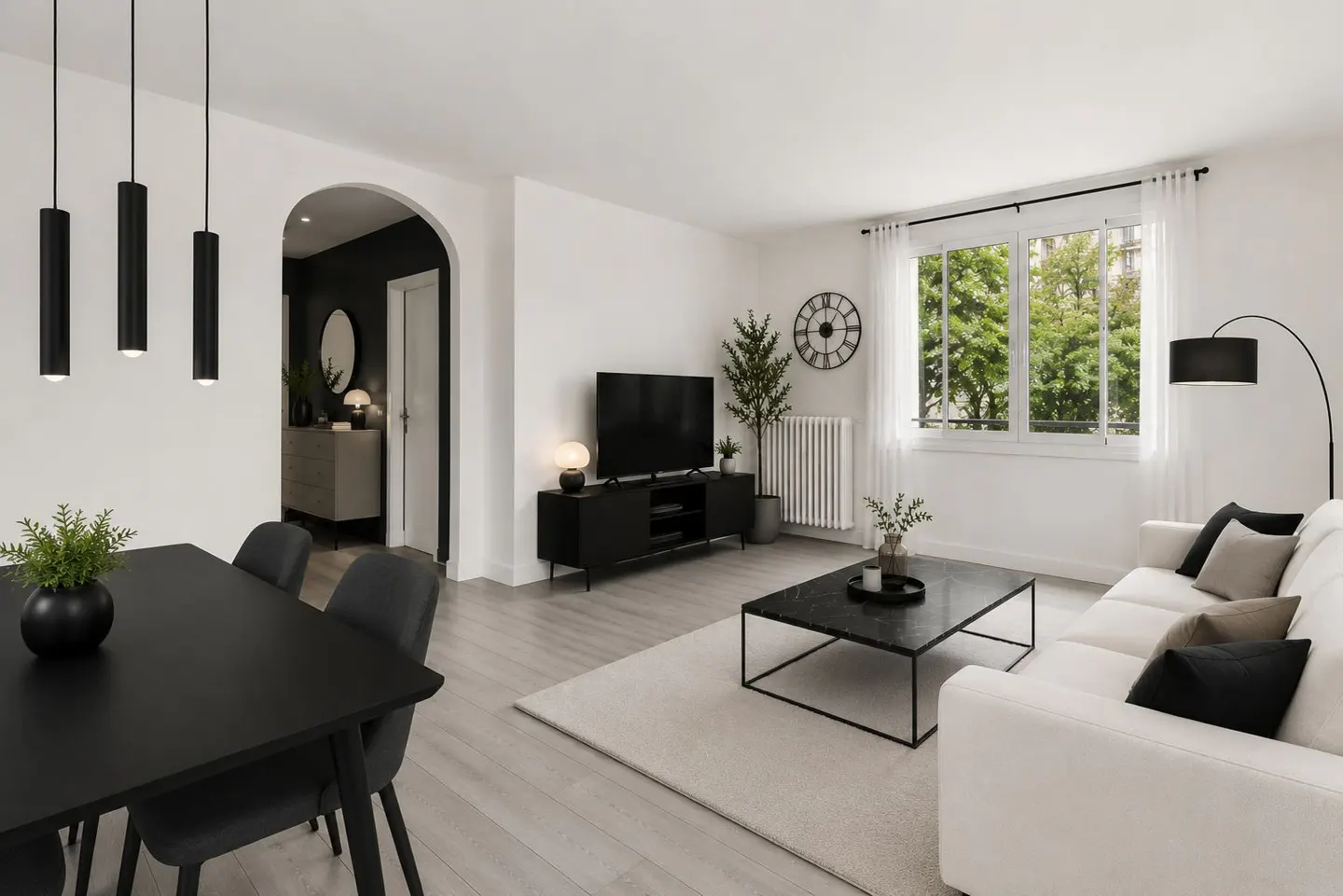 Bright living room with white walls, light wood floors, and black accents. A black dining table sits near a white sofa and TV stand.