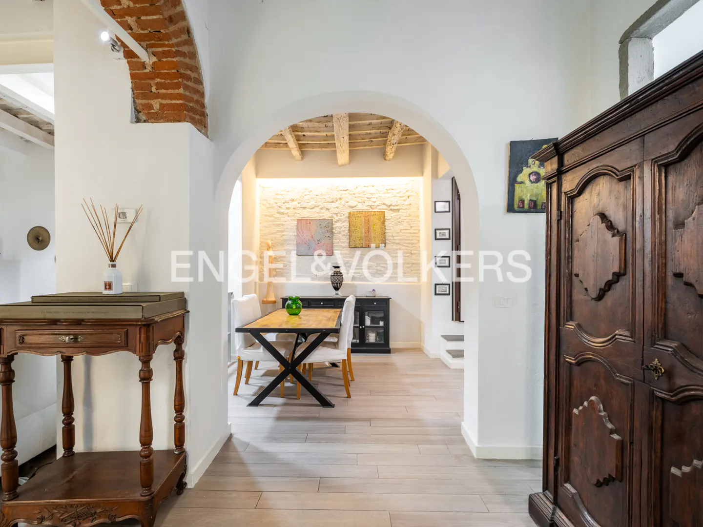 Interior view of a home with white walls, wooden floors, and an arched doorway leading to a dining area.
