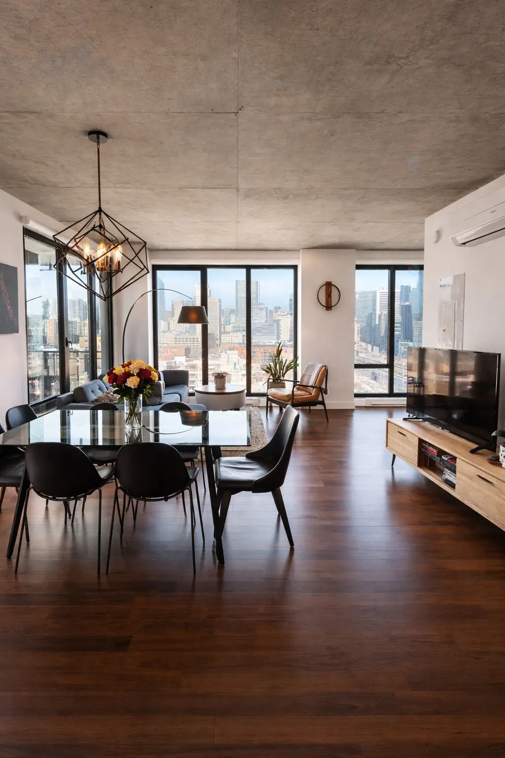 A modern apartment interior with a dining table, chairs, and a city view through large windows.