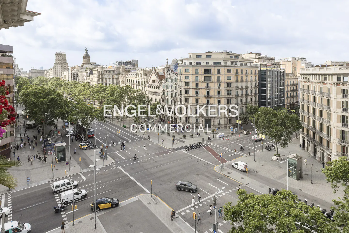 High-angle view of a busy Barcelona street intersection with historic buildings, trees, pedestrians, and city traffic.