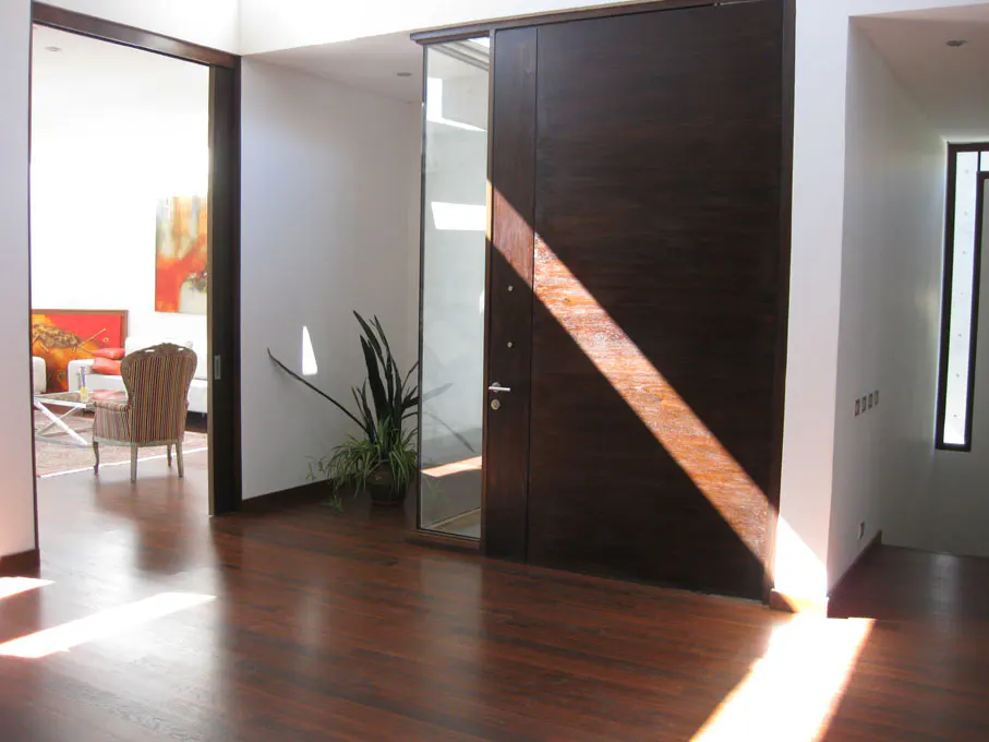 Hallway with dark wood floors, a large dark wood door with glass panel, and a view into a living room with colorful art.