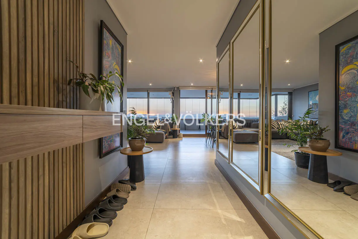 Hallway view with light tile floor, wood accent wall, and large mirrors reflecting the living room with city views.