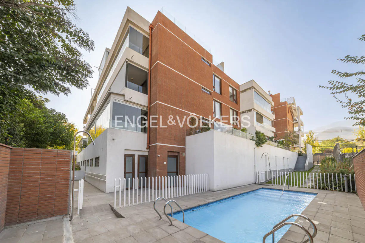 Exterior view of a modern brick and white apartment building with a blue swimming pool in the foreground.