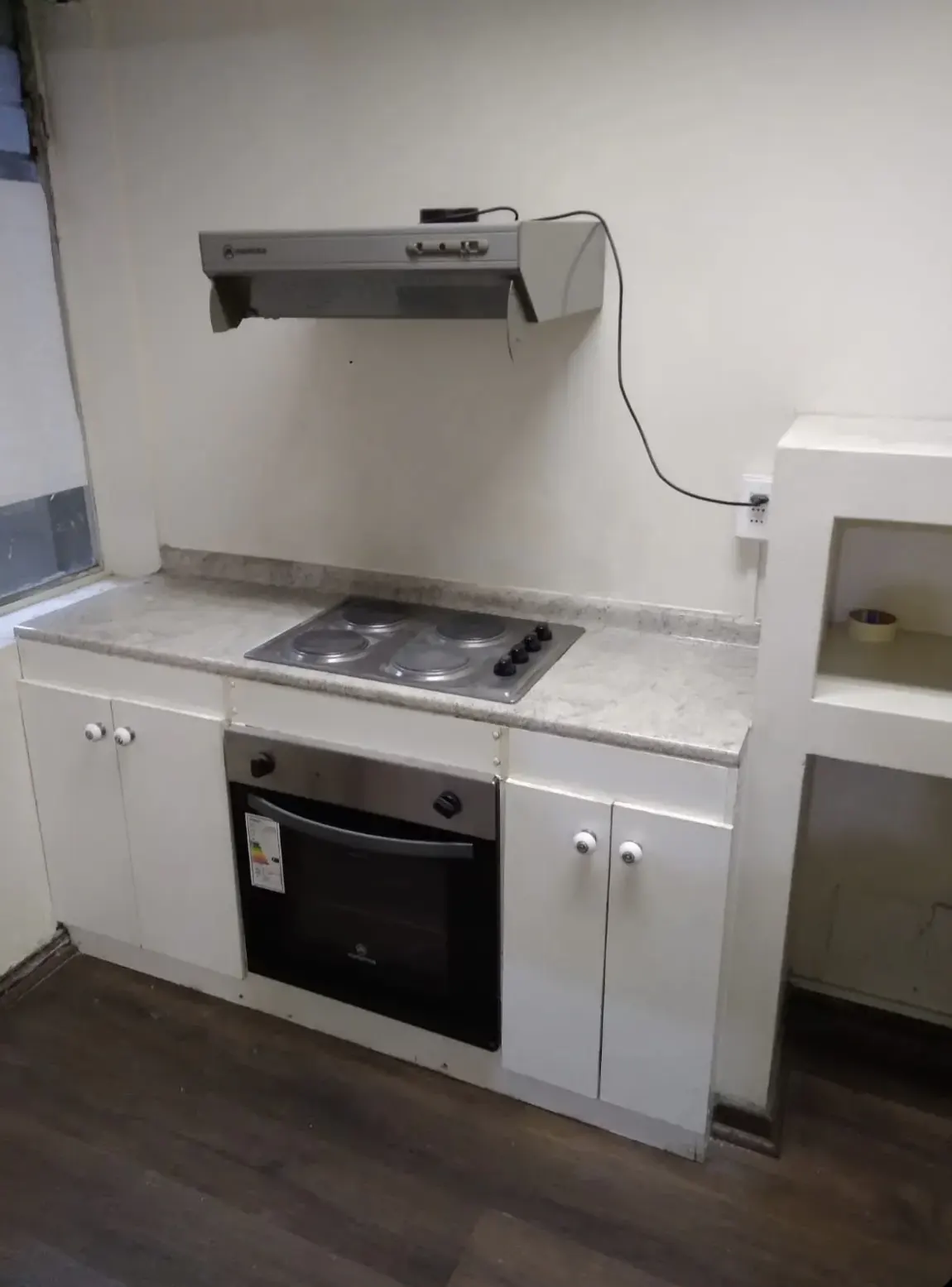 A kitchen with white cabinets, a gray countertop, and a black oven. A gray range hood is mounted on the wall above the stove.