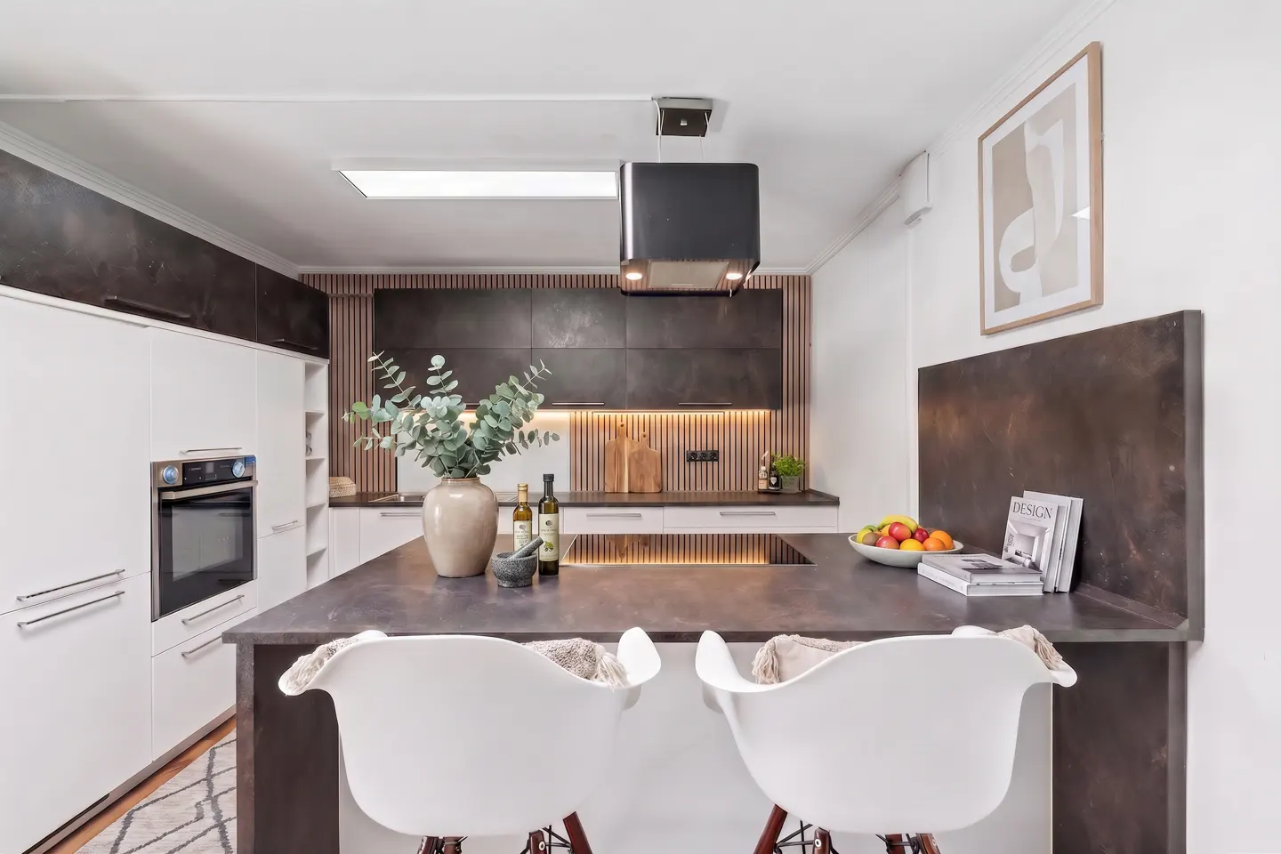 Modern kitchen with white cabinets, dark countertops, a central island with two white chairs, and wood-slat wall accents.